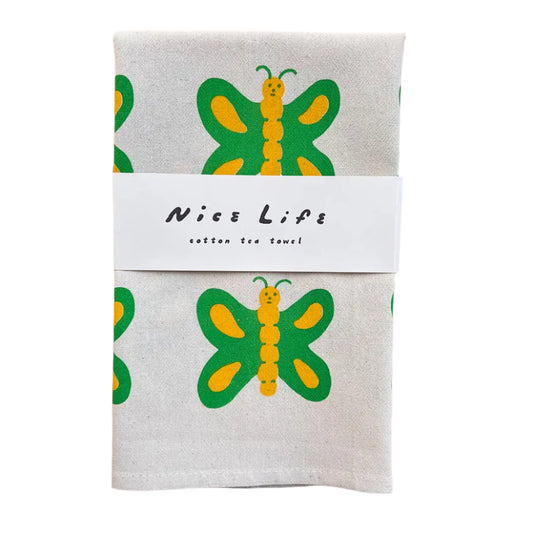 Tea towel with green butterfly design and 'Nice Life' label on a wooden surface
