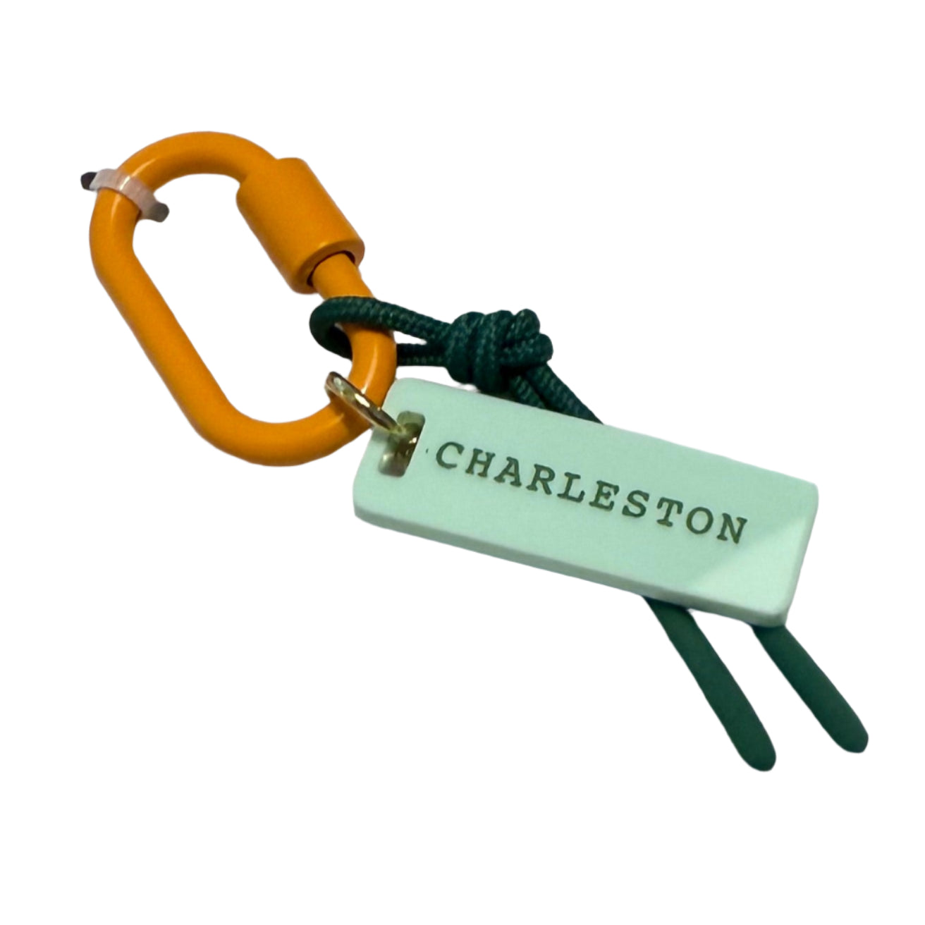 Bag charm with green tag and orange clip on a white card with blue border on wooden surface