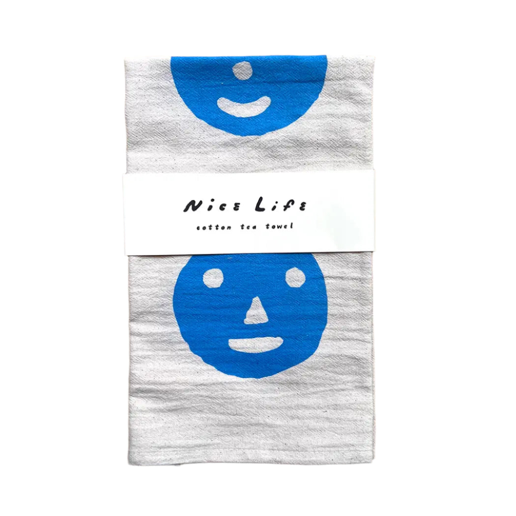 Gray tea towel with blue smiley face design and 'Nice Life' label on a wooden surface